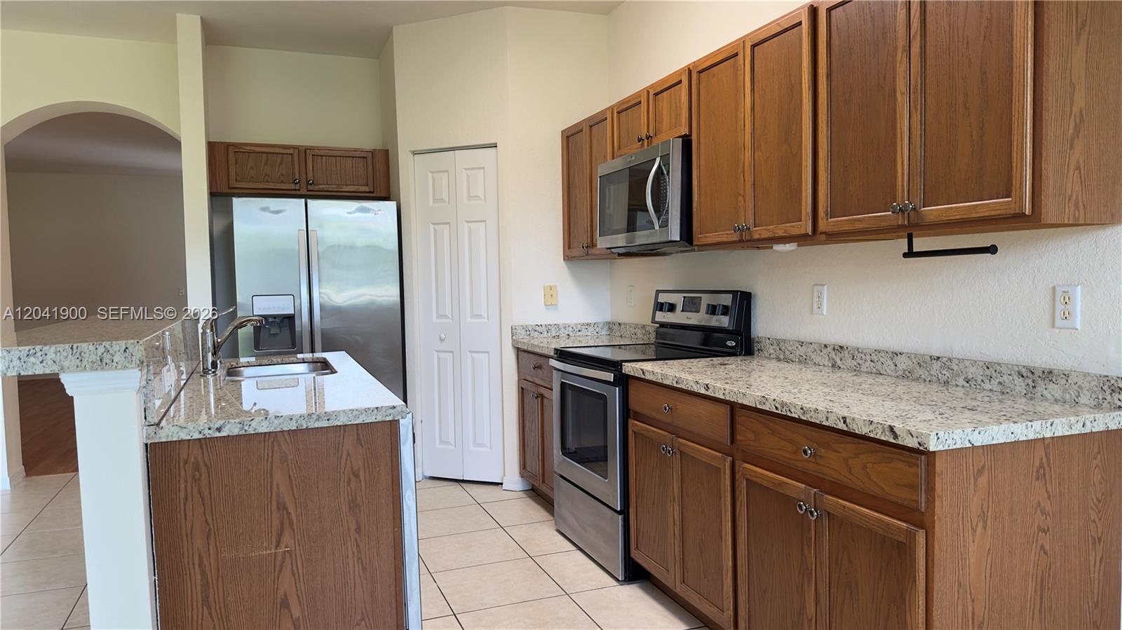A kitchen features wood cabinets, granite countertops, stainless steel appliances, and tile flooring — 3042 Grandiflora Dr, Green Acres FL 33467, GREEN ACRES, FL
