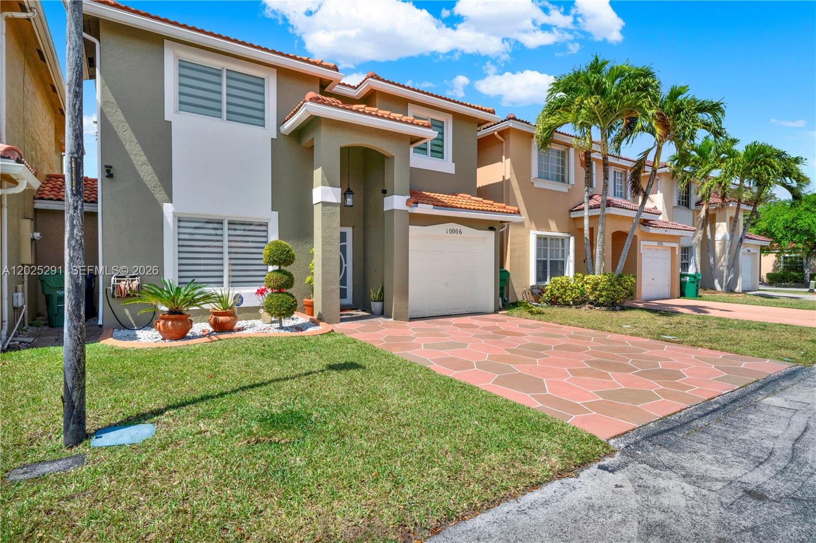 A two-story house with a paved driveway, garage, and green lawn under a blue sky — 10006 SW 162nd Path, Miami FL 33196, MIAMI, FL