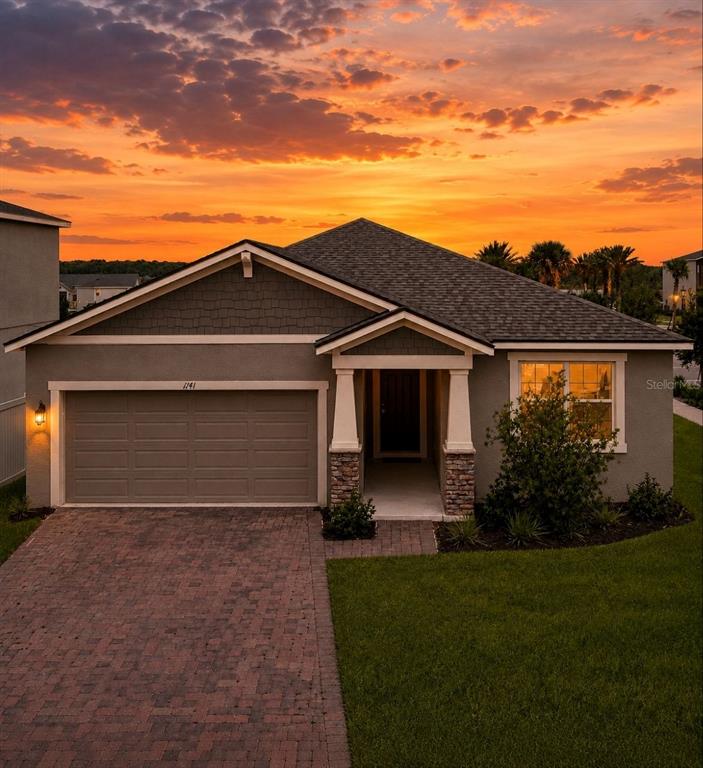 A single-story house with a gray stucco exterior, stone accents, and a brick paver driveway — 1141 LAKESHORE BREEZE PLACE, KISSIMMEE, FL