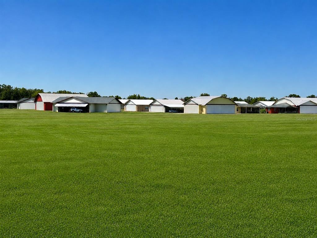 A large, grassy field sits in front of a row of airplane hangars — GRASS ROOTS ROAD, GROVELAND, FL