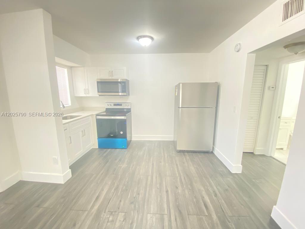 A kitchen features white cabinets, stainless steel appliances, and light-colored wood-look flooring — 2150 NW 24th St # 2, Miami FL 33142, MIAMI, FL