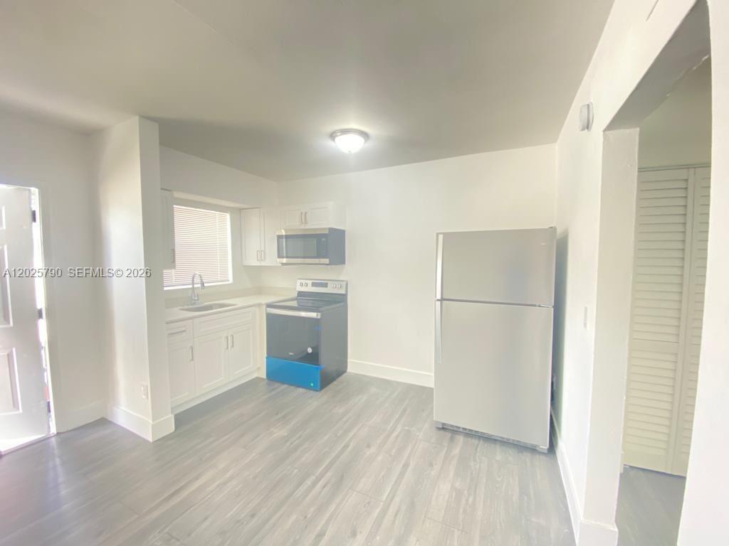 A kitchen features white cabinets, stainless steel appliances, and light gray wood-look flooring — 2150 NW 24th St # 2, Miami FL 33142, MIAMI, FL