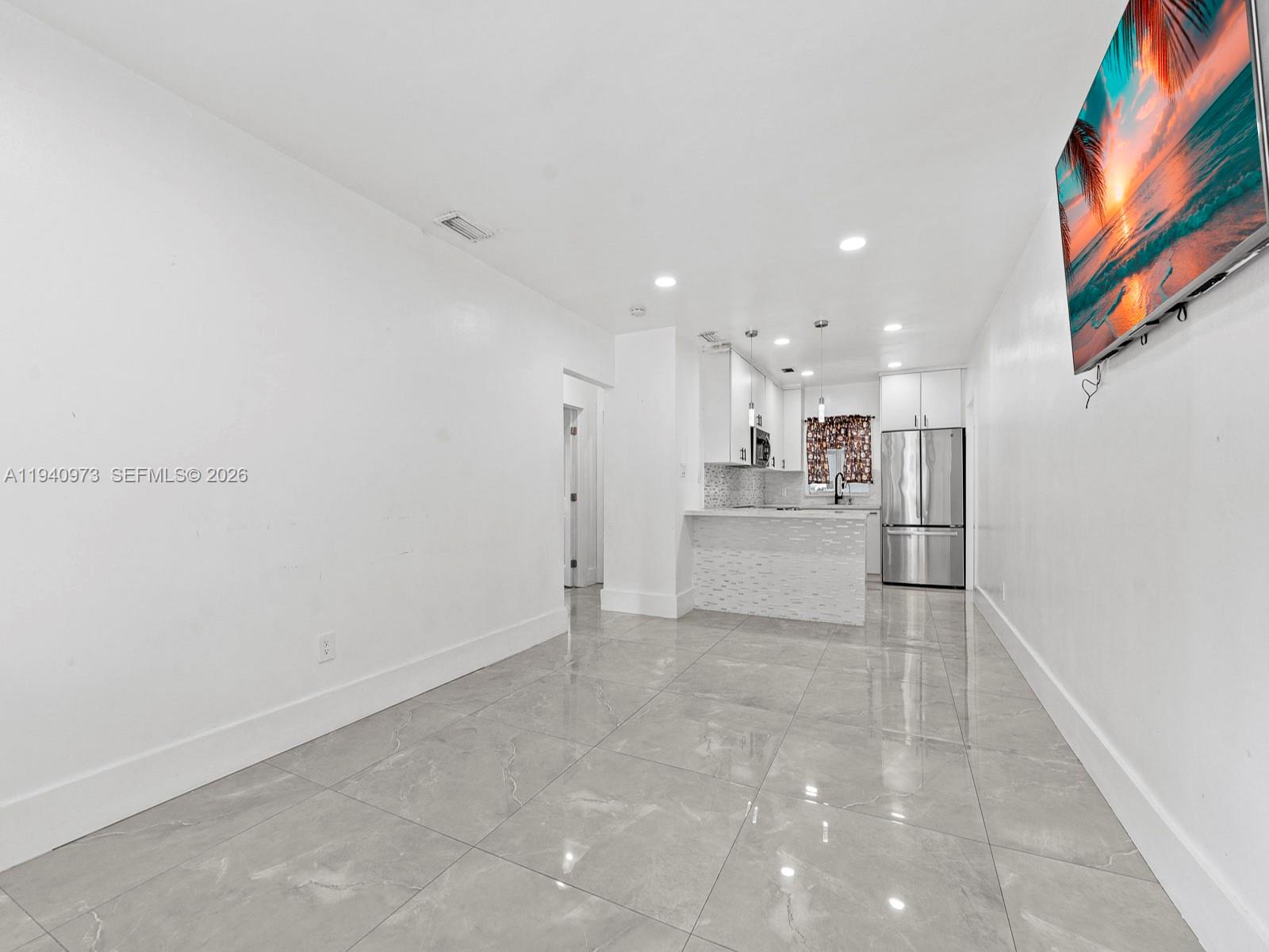A bright, open-concept living area features large gray tile flooring and a modern kitchen — 1230 NW 35th St, Miami FL 33142, MIAMI, FL