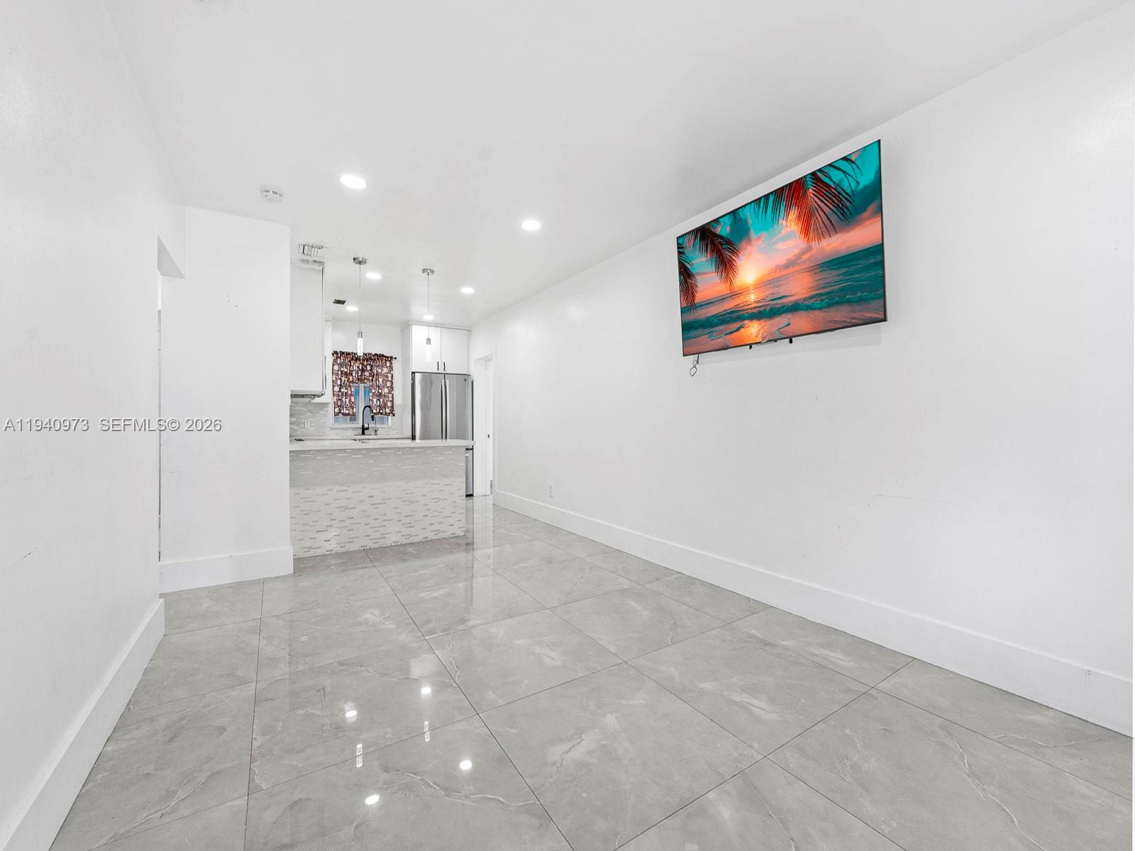 A bright, minimalist living area features large gray floor tiles and a wall-mounted television — 1230 NW 35th St, Miami FL 33142, MIAMI, FL