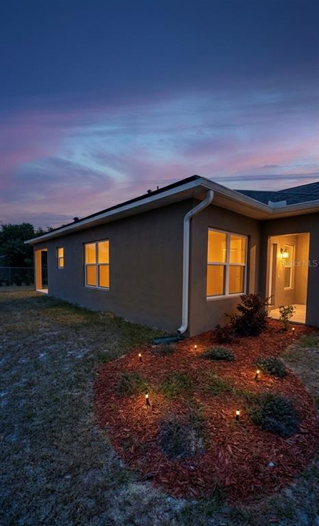 The exterior of a house at dusk features a brown stucco wall, windows, and landscaping — 4123 MANDARIN ROAD, SEBRING, FL