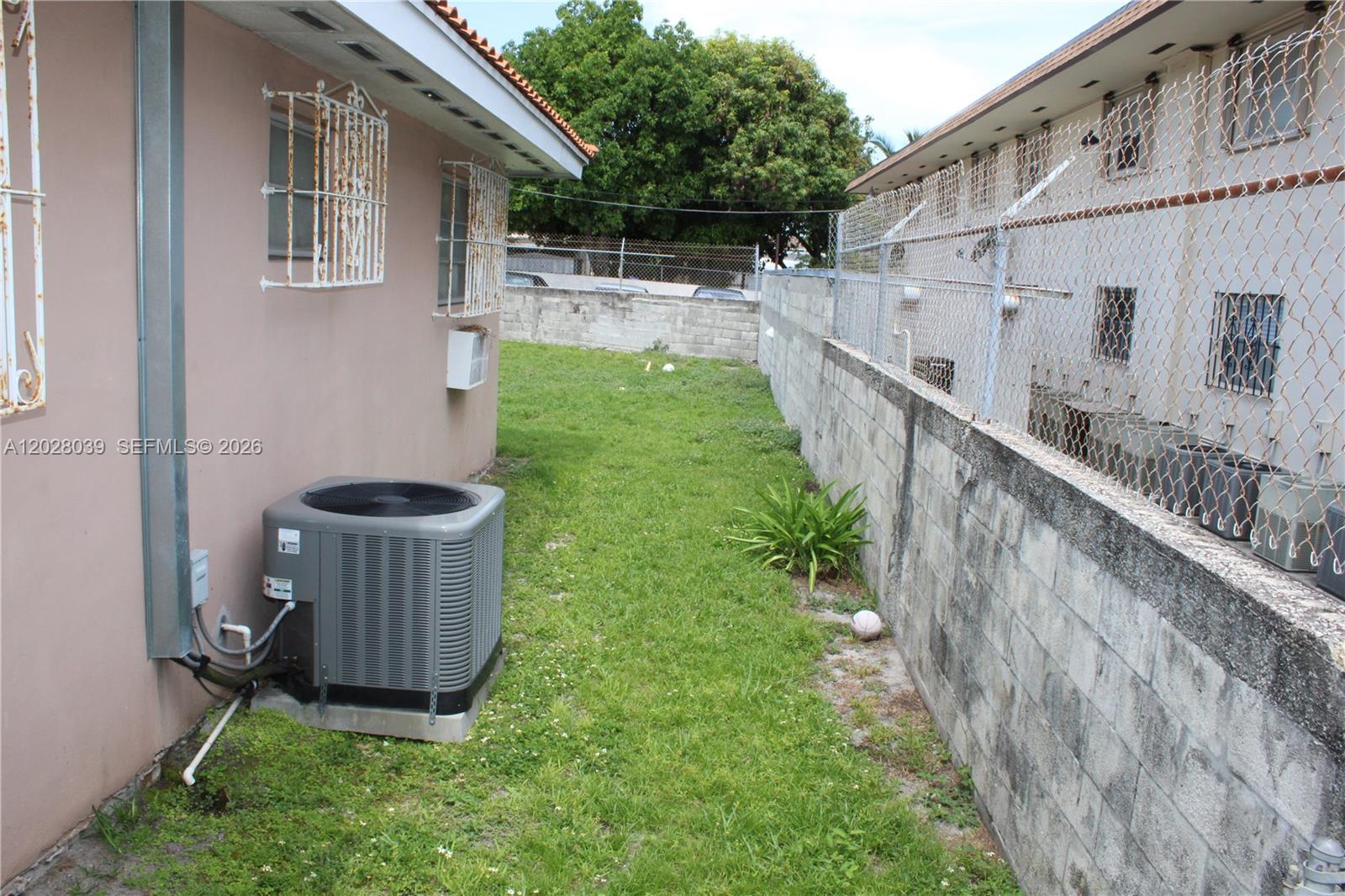 A narrow grassy side yard sits between a house with an air conditioner and a wall — 1040 NW 23rd Ct, Miami FL 33125, MIAMI, FL