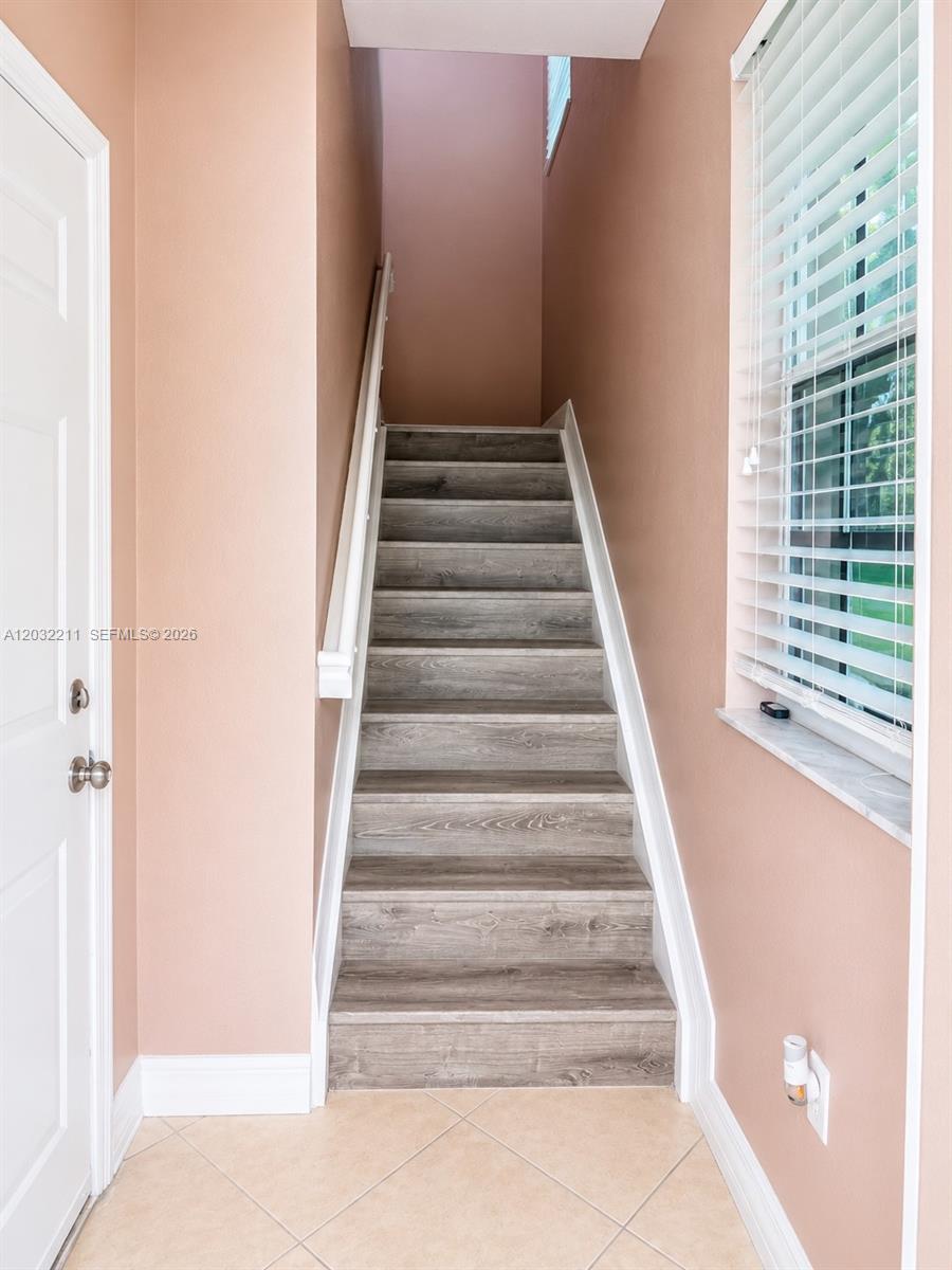 A staircase with wood-look treads leads upward between peach-colored walls and a tiled floor — 13221 SW 42nd St # 8203, Miramar FL 33027, MIRAMAR, FL