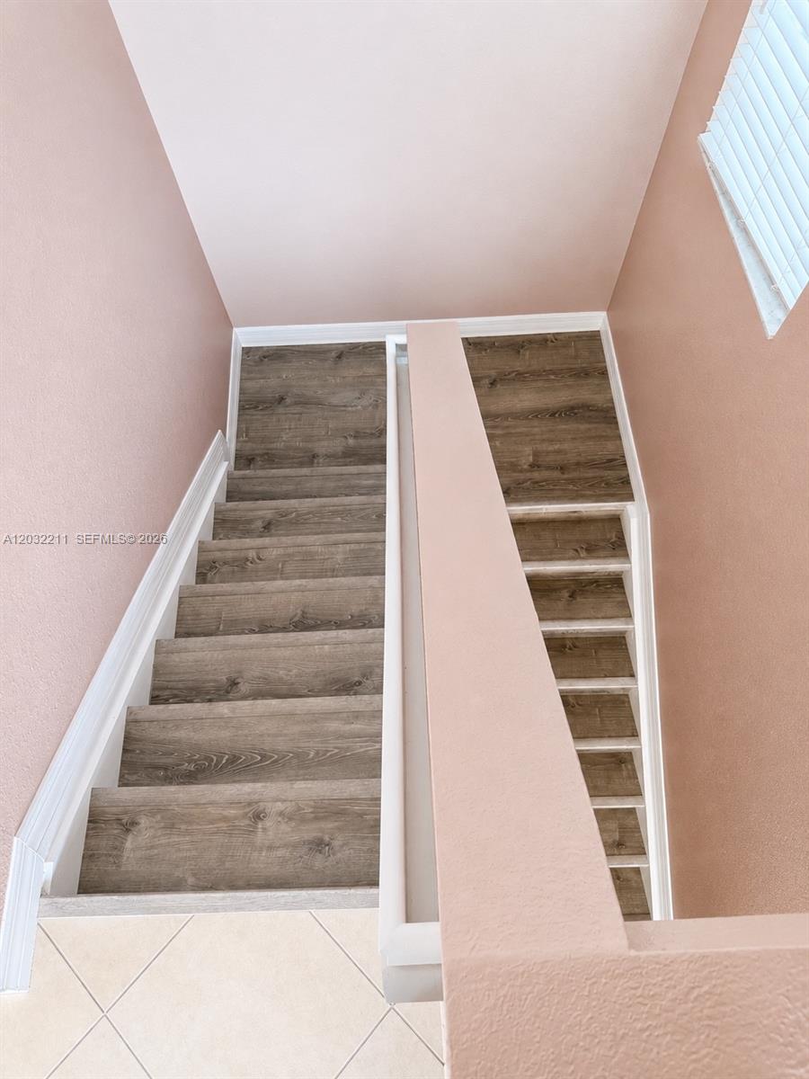 A staircase with wood-look flooring and a pink wall descends to a tiled floor — 13221 SW 42nd St # 8203, Miramar FL 33027, MIRAMAR, FL