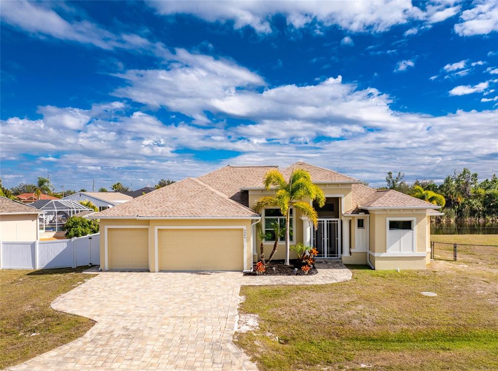 A single-story yellow house with a paver driveway, three-car garage, and a palm tree — 9386 ARRID CIRCLE, PORT CHARLOTTE, FL