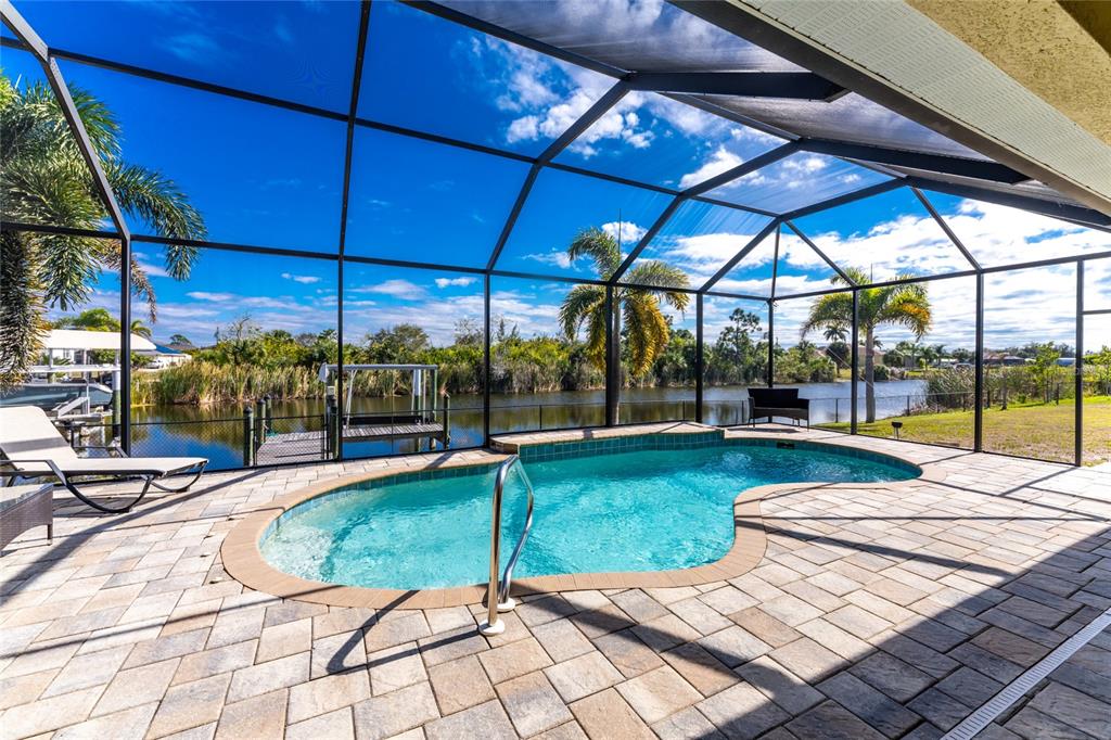 A screened-in patio features a kidney-shaped swimming pool, paver deck, and a view of water — 9386 ARRID CIRCLE, PORT CHARLOTTE, FL