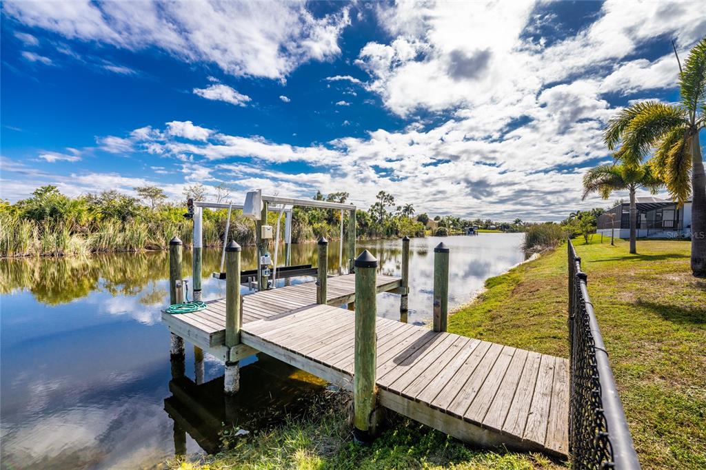 A wooden boat dock with a lift extends into a calm canal under a cloudy sky — 9386 ARRID CIRCLE, PORT CHARLOTTE, FL