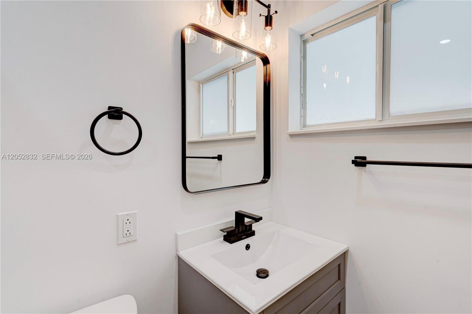 A bathroom features a gray vanity, black faucet, rectangular mirror, and black wall-mounted hardware — 3635 SW 88th Ct, Miami FL 33165, MIAMI, FL
