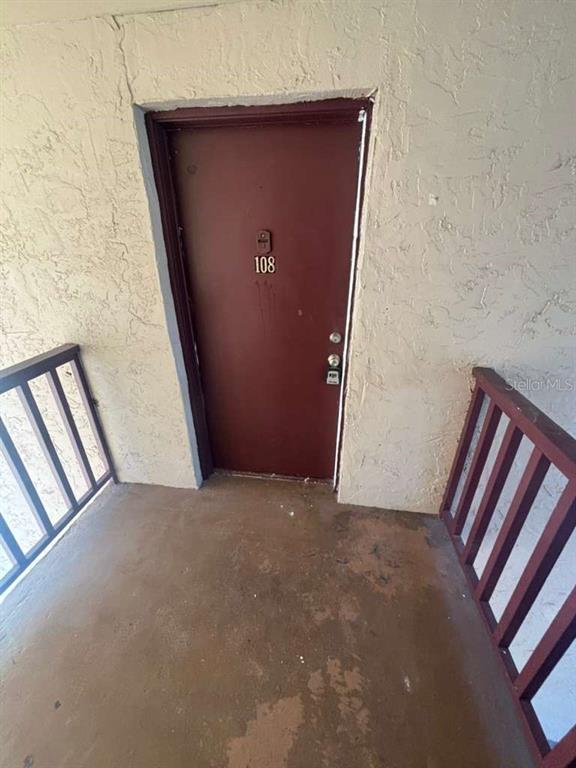 A brown apartment door labeled 108 is situated on a concrete balcony with railings — 3824 N LAKE DRIVE UNIT 108, TAMPA, FL