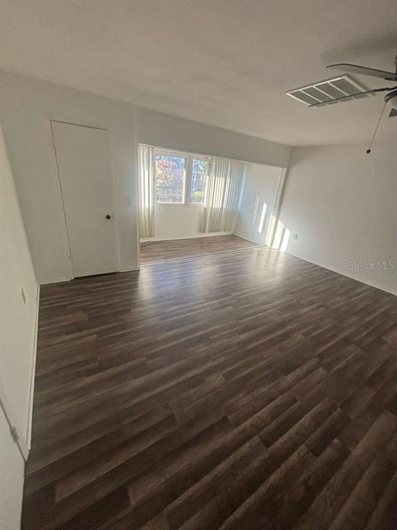 An empty room with dark wood-look flooring, white walls, a ceiling fan, and large windows — 3824 N LAKE DRIVE UNIT 108, TAMPA, FL