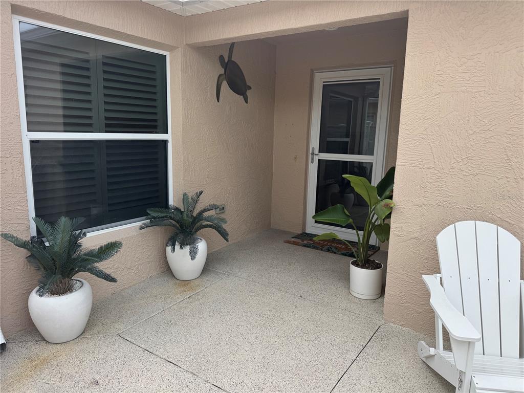 A covered patio features a white door, three potted plants, and a white Adirondack chair — 1946 MCCONNELLS AVENUE, THE VILLAGES, FL