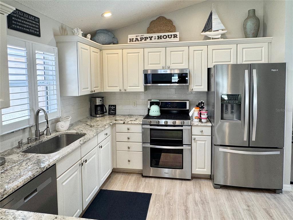 A kitchen features white cabinets, granite countertops, stainless steel appliances, and light wood-look flooring — 1946 MCCONNELLS AVENUE, THE VILLAGES, FL