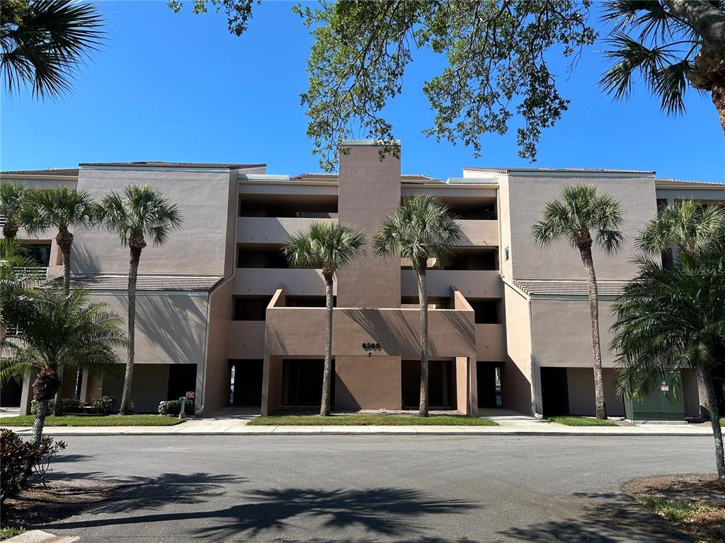 A multi-story tan apartment building features palm trees and a central entrance with number 6260 — 6260 KIPPS COLONY COURT UNIT 203, GULFPORT, FL