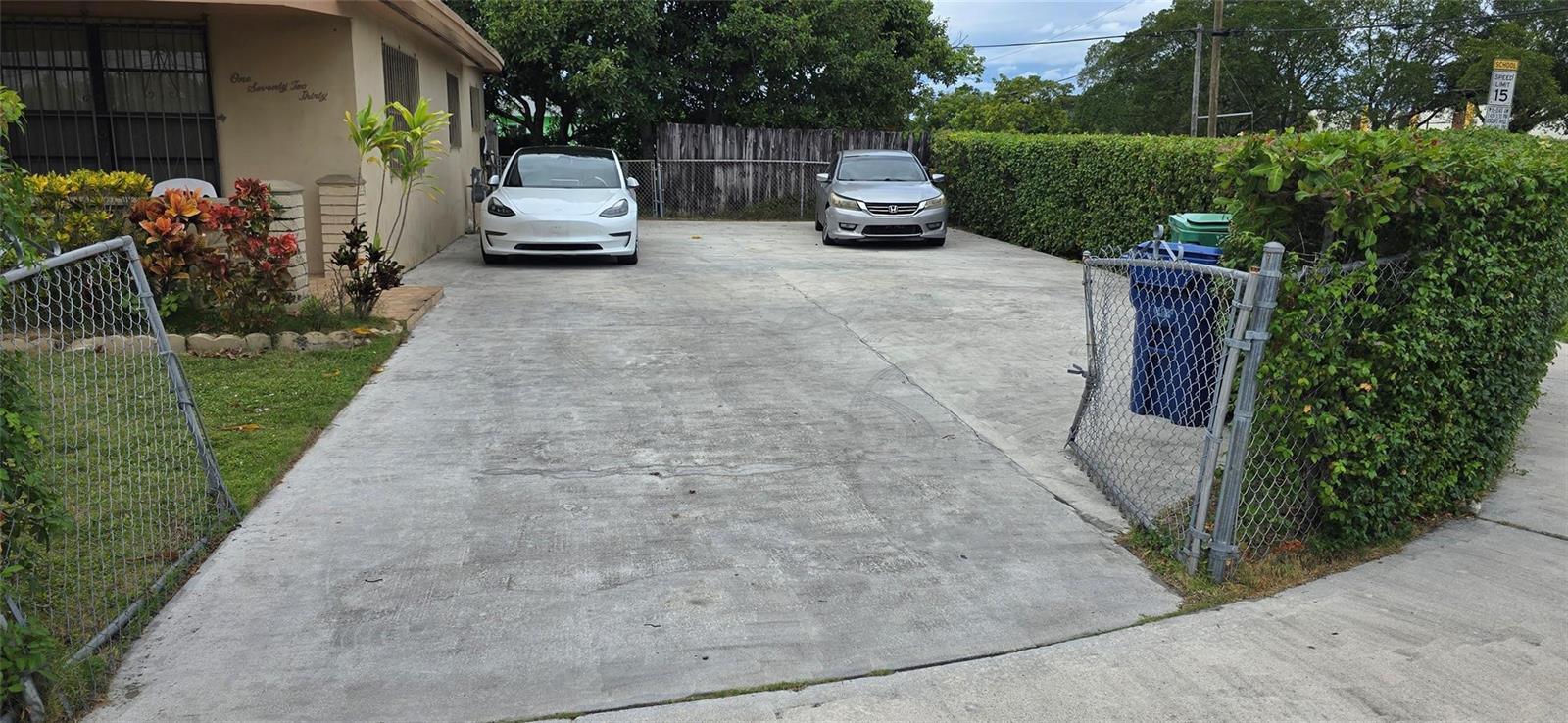 A concrete driveway leads to a house with two parked cars and a chain-link fence — 17230 NW 10th Court, Miami FL 33169, MIAMI, FL