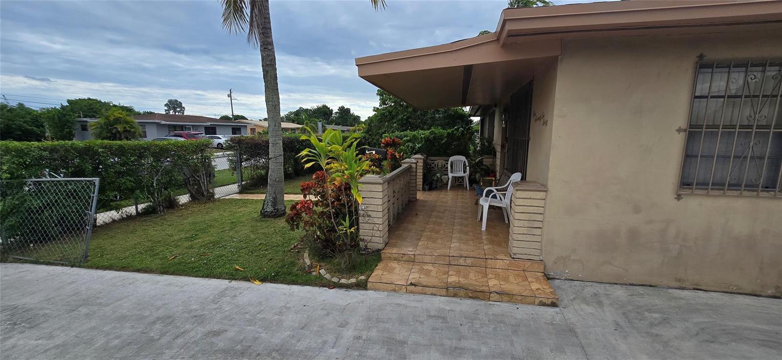 A tiled front porch with a brick wall and white chairs sits beside a house — 17230 NW 10th Court, Miami FL 33169, MIAMI, FL