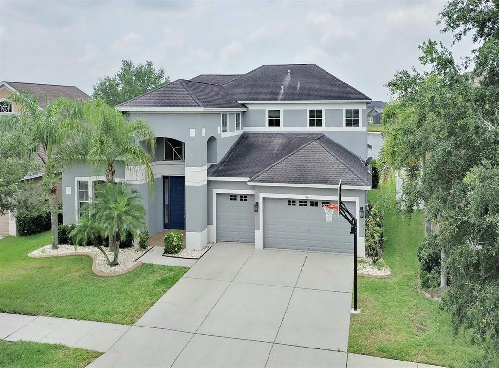A two-story gray house with a dark roof, a three-car garage, and a basketball hoop — 13714 ARTESA BELL DRIVE, RIVERVIEW, FL