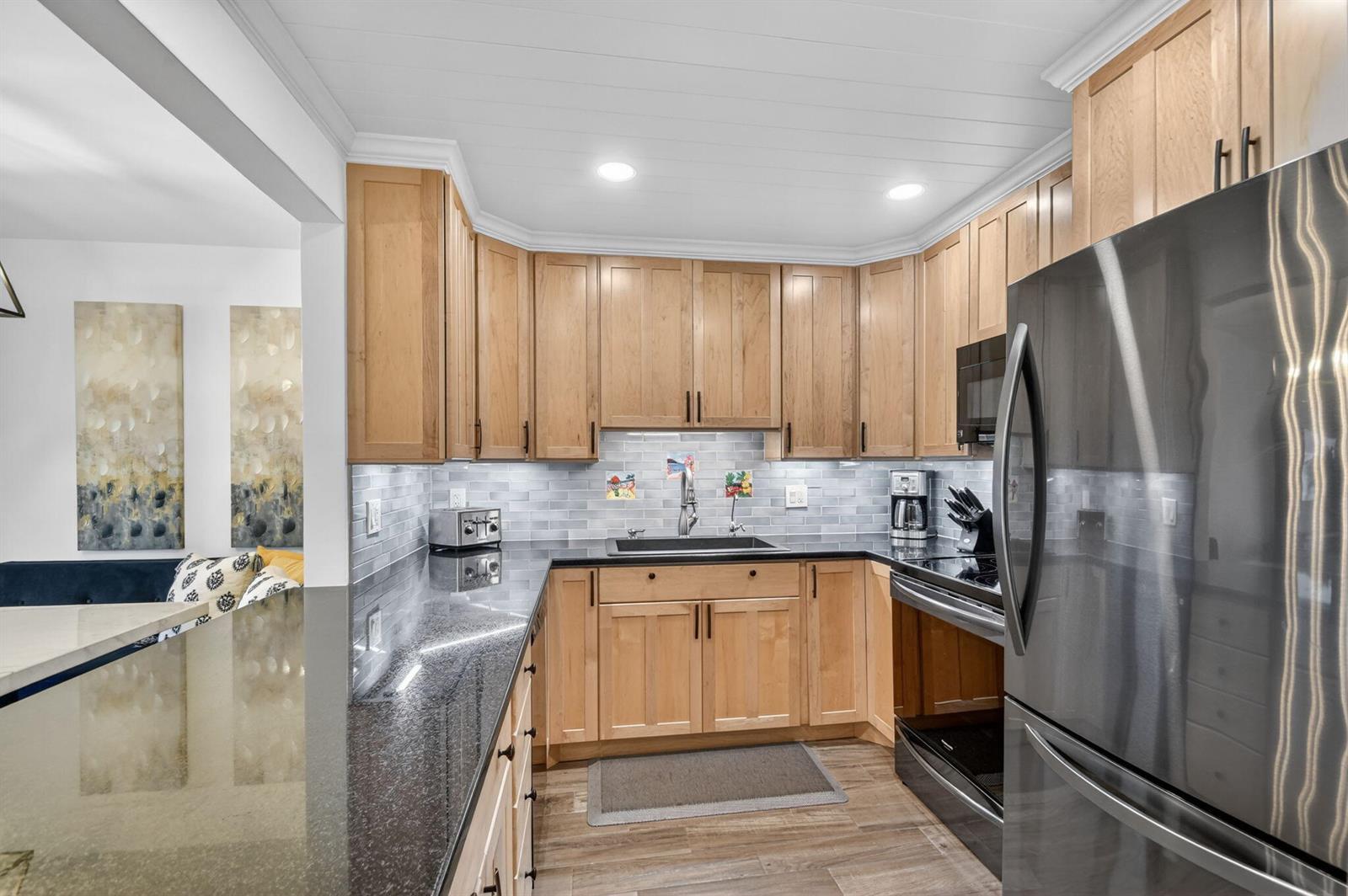 A kitchen features light wood cabinets, black granite countertops, and a gray subway tile backsplash — 1502 S Lakeside Drive # 214, FL 33460, FL