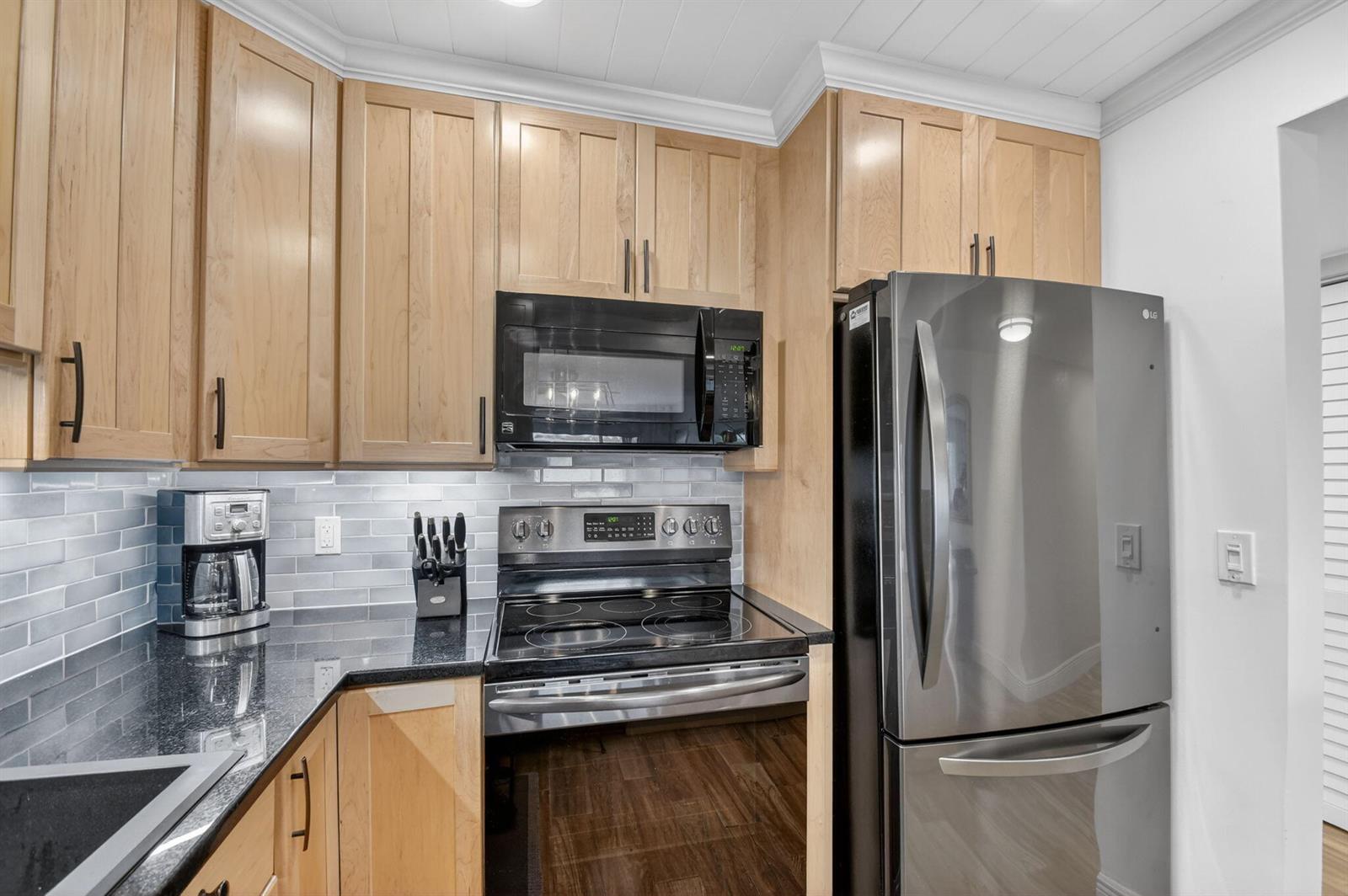 A kitchen features light wood cabinets, black granite countertops, stainless steel appliances, and gray tile — 1502 S Lakeside Drive # 214, FL 33460, FL