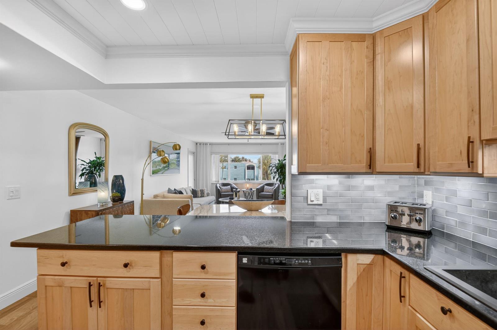 A kitchen with light wood cabinets and black countertops overlooks a living area with furniture — 1502 S Lakeside Drive # 214, FL 33460, FL