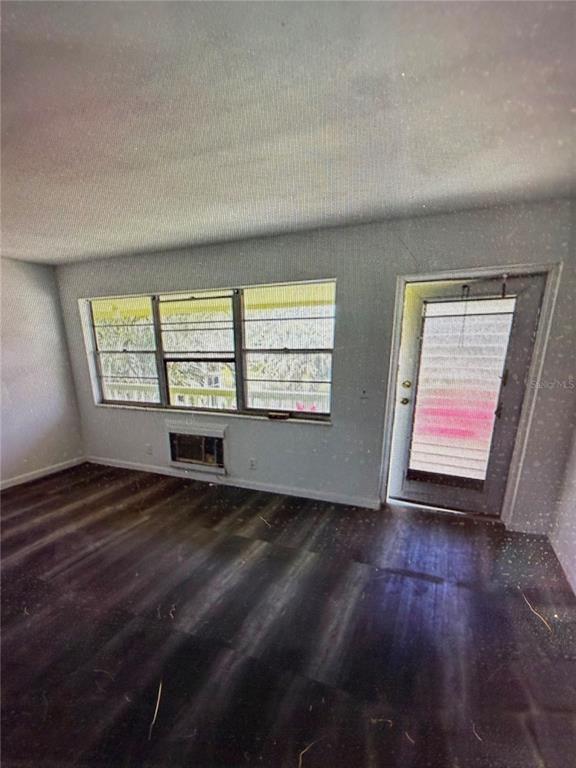 An empty room with dark wood-look flooring, a window, a wall-mounted air conditioner, and a door — 42 SHEFFIELD B UNIT B, WEST PALM BEACH, FL
