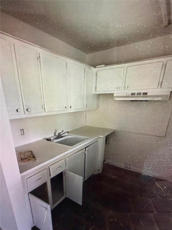 A small kitchen features white cabinets, a stainless steel sink, and dark tiled flooring — 42 SHEFFIELD B UNIT B, WEST PALM BEACH, FL