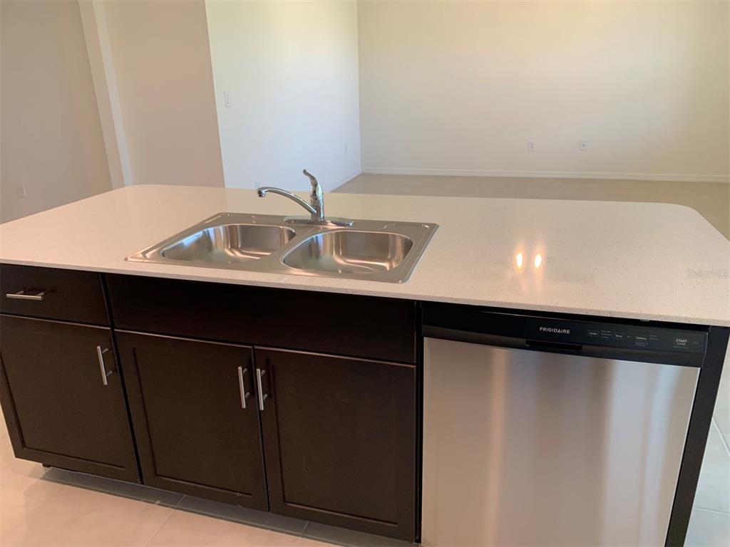 A kitchen island features a stainless steel sink, dark cabinets, and a light-colored countertop — 341 TANDIL STREET, PUNTA GORDA, FL
