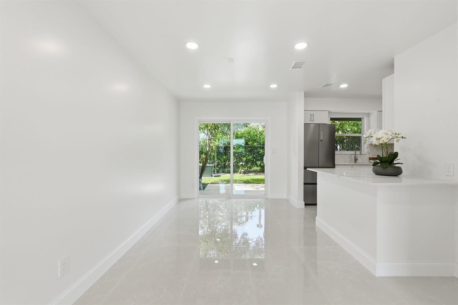 A bright, minimalist dining area features white walls, glossy tile floors, and a sliding glass door — 6505 Dockside Circle, FL 33463, FL