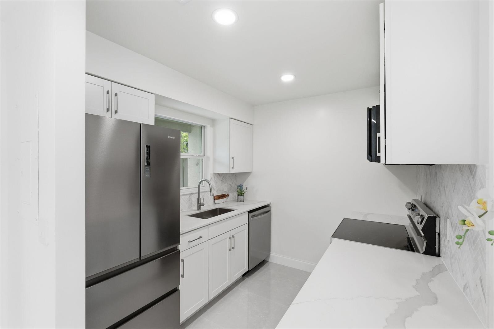 A modern kitchen features white cabinets, stainless steel appliances, and light-colored countertops — 6505 Dockside Circle, FL 33463, FL