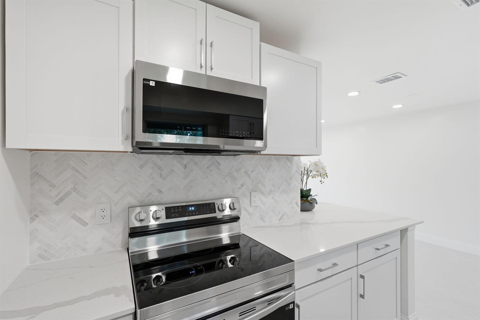 A modern kitchen features white cabinets, stainless steel appliances, and a herringbone marble backsplash — 6505 Dockside Circle, FL 33463, FL