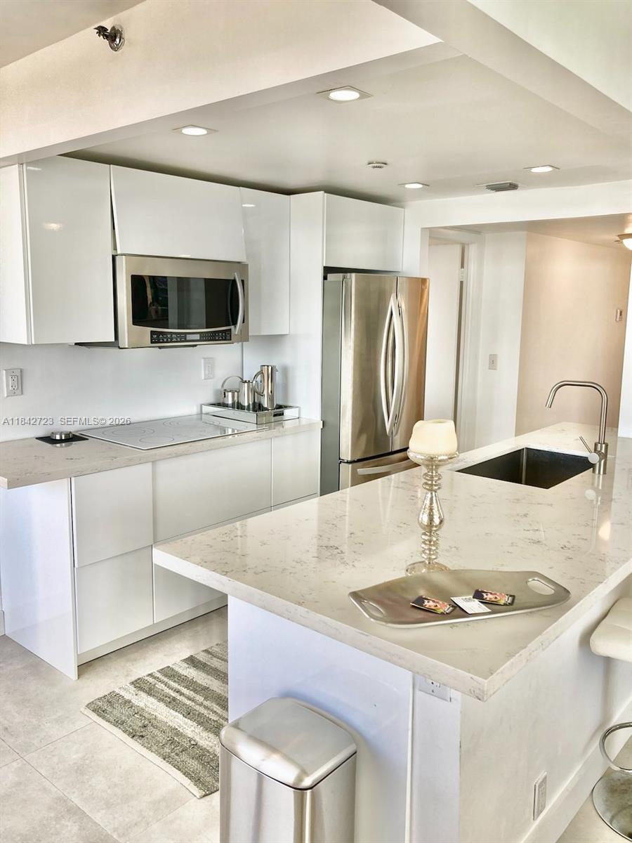 A modern kitchen features white cabinetry, a stainless steel refrigerator, and a view of buildings — 2555 Collins Ave, Miami Beach FL 33140, MIAMI BEACH, FL