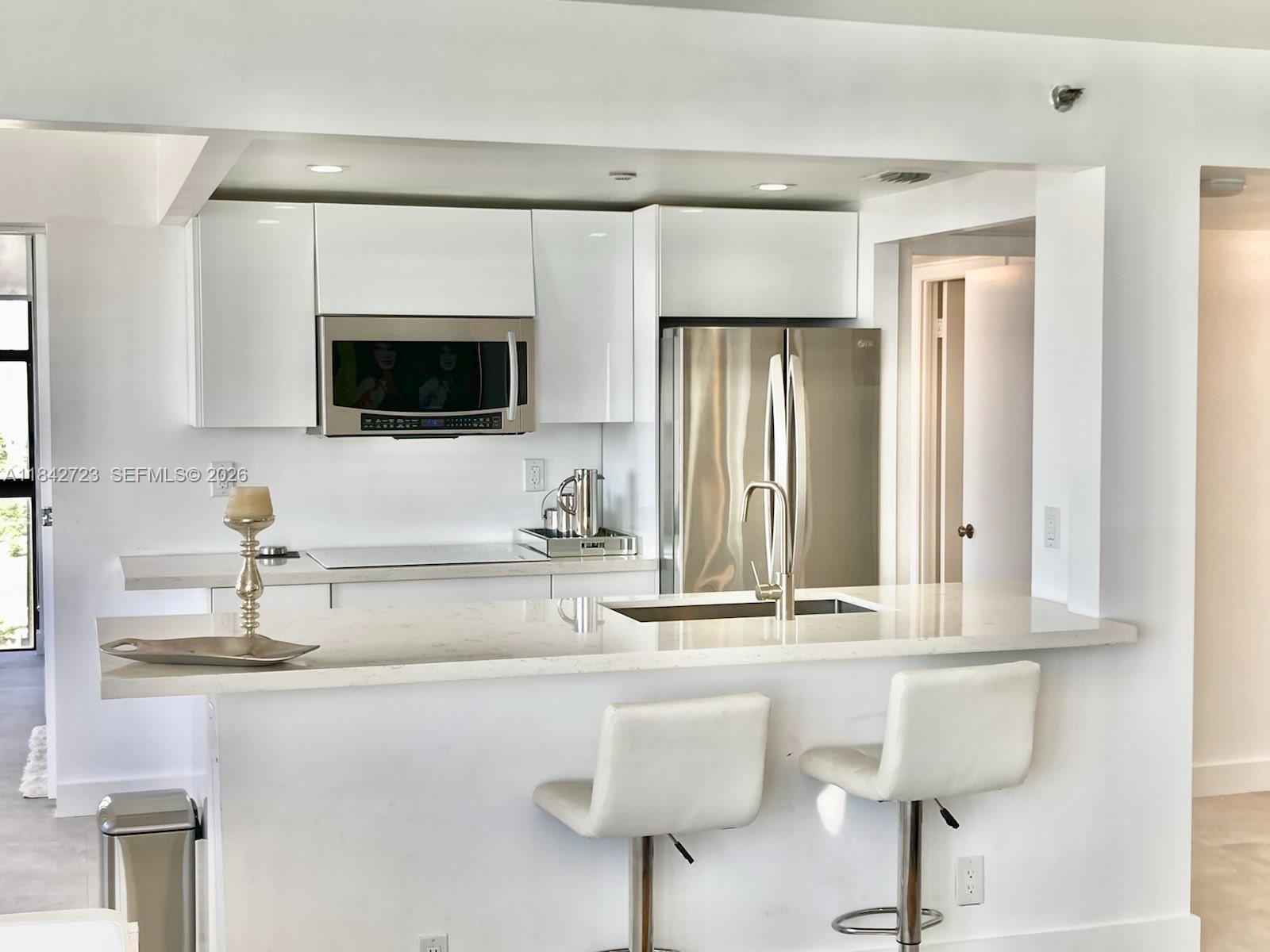 A modern kitchen features white cabinets, stainless steel appliances, and a quartz-topped island — 2555 Collins Ave, Miami Beach FL 33140, MIAMI BEACH, FL