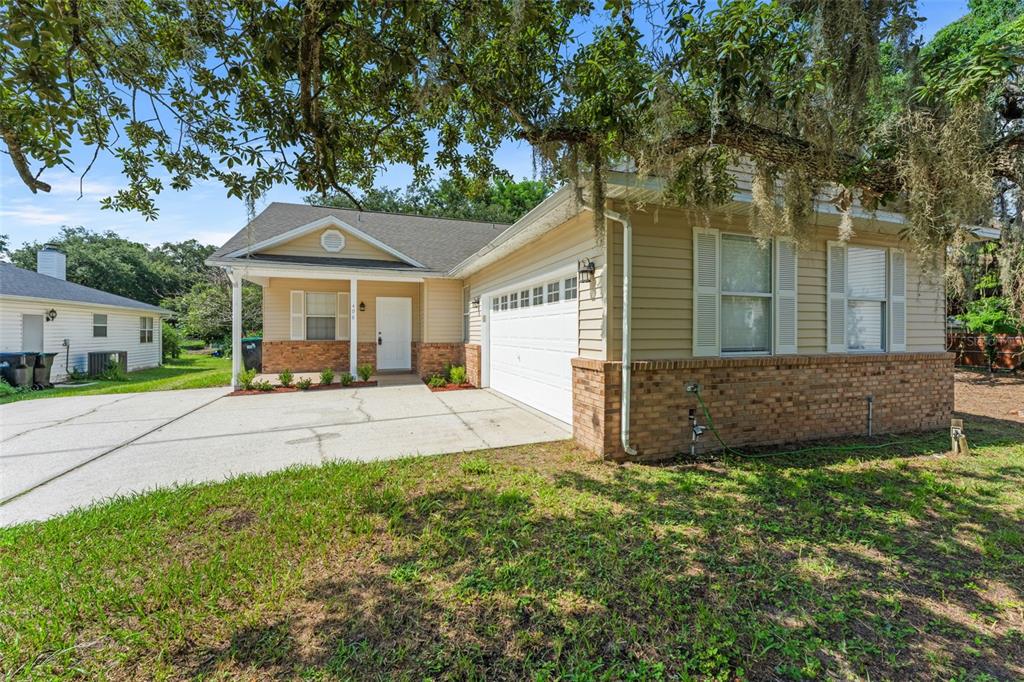 A single-story house with tan siding, a brick base, a white garage door, and driveway — 498 DEAN CREEK LANE, ORLANDO, FL
