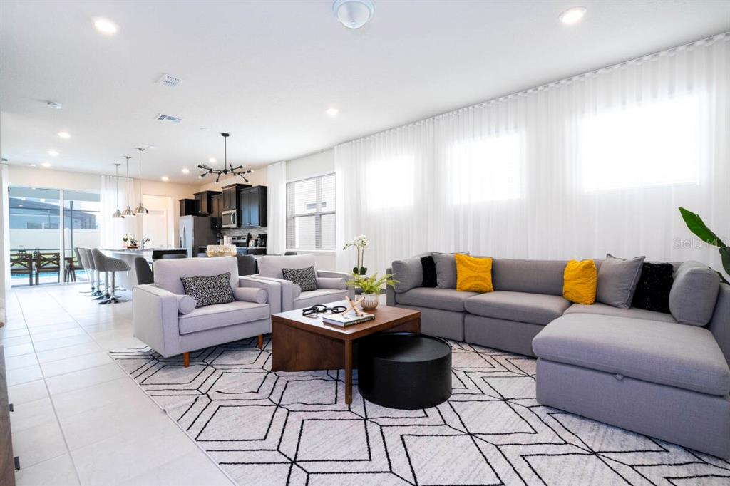 A modern open-concept living room features a gray sectional, two armchairs, and a geometric rug — 3428 LILAC WAY, DAVENPORT, FL