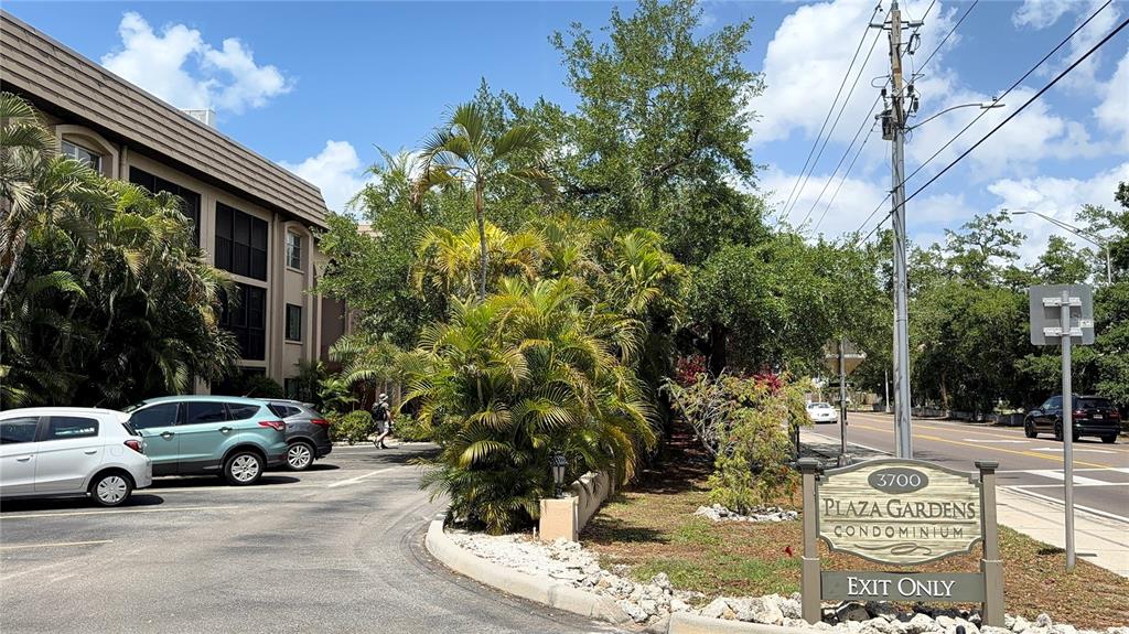 A sign for Plaza Gardens Condominium stands near a parking lot with several parked cars — 3700 S OSPREY AVENUE UNIT 205, SARASOTA, FL