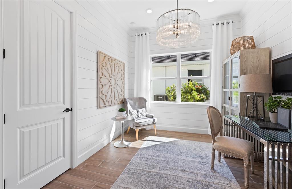 A home office features white shiplap walls, a crystal chandelier, and a glass-topped desk — 10362 BLUE RUNNER DRIVE, ENGLEWOOD, FL
