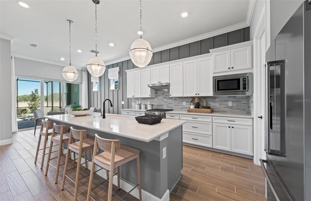 A modern kitchen features a large island with bar seating, white cabinetry, and gray walls — 10362 BLUE RUNNER DRIVE, ENGLEWOOD, FL