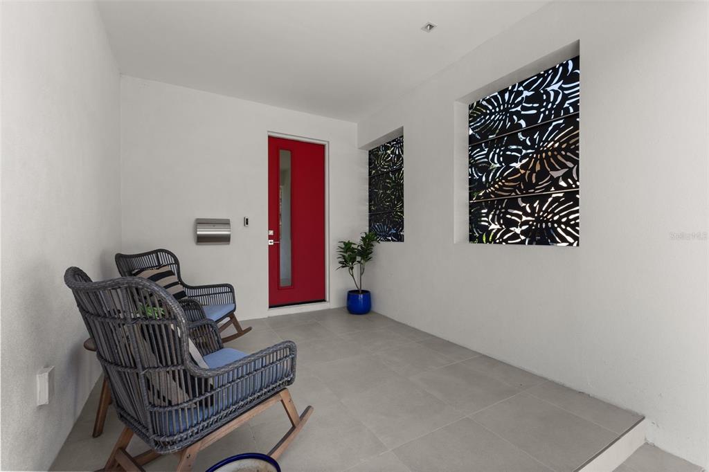 A covered entryway features gray tile flooring, two wicker rocking chairs, and a bright red door — 668 NEWTON AVENUE S, ST PETERSBURG, FL