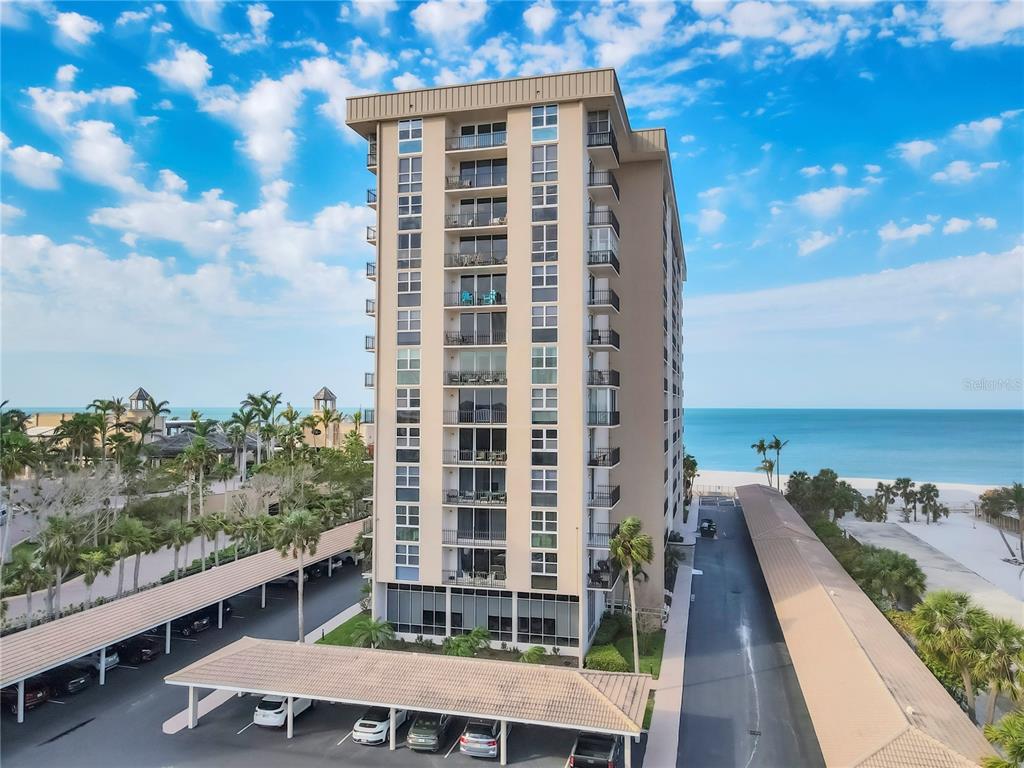An exterior view of a tall beachfront condominium building with covered parking structures below — 1212 BENJAMIN FRANKLIN DRIVE UNIT 508, SARASOTA, FL