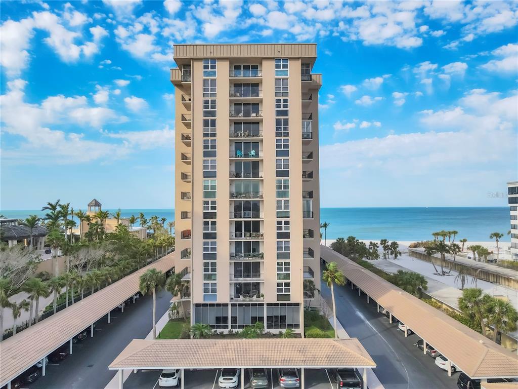 An aerial view shows a tall tan residential building situated between parking structures and beach — 1212 BENJAMIN FRANKLIN DRIVE UNIT 508, SARASOTA, FL