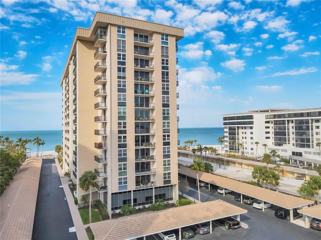 An exterior view of a tall, tan beachfront condominium building with covered parking below — 1212 BENJAMIN FRANKLIN DRIVE UNIT 508, SARASOTA, FL