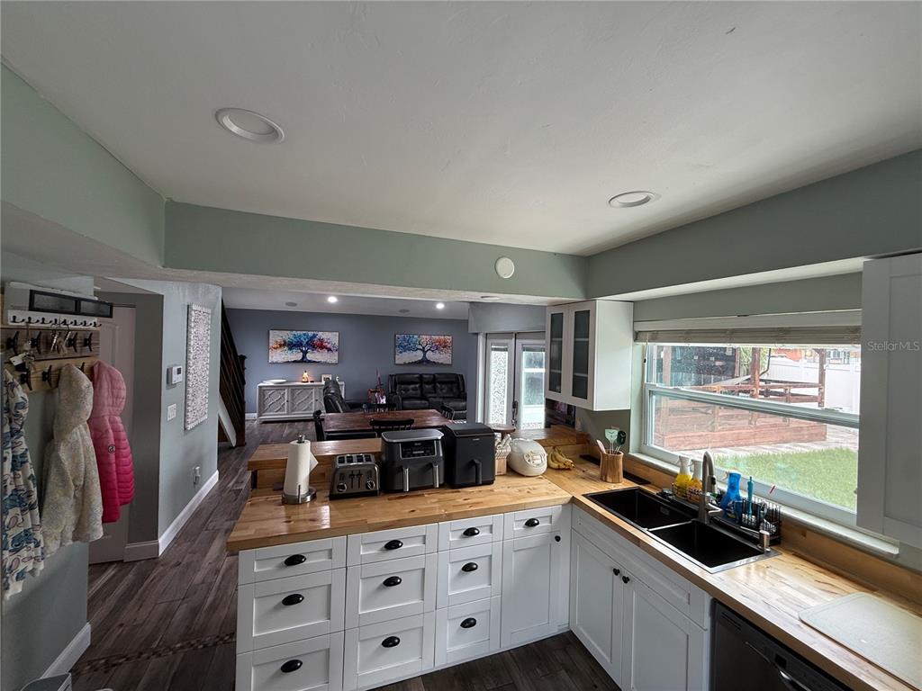 A kitchen with white cabinets and wood countertops opens into a living and dining area — 10009 REGAL WOODS LANE, TAMPA, FL