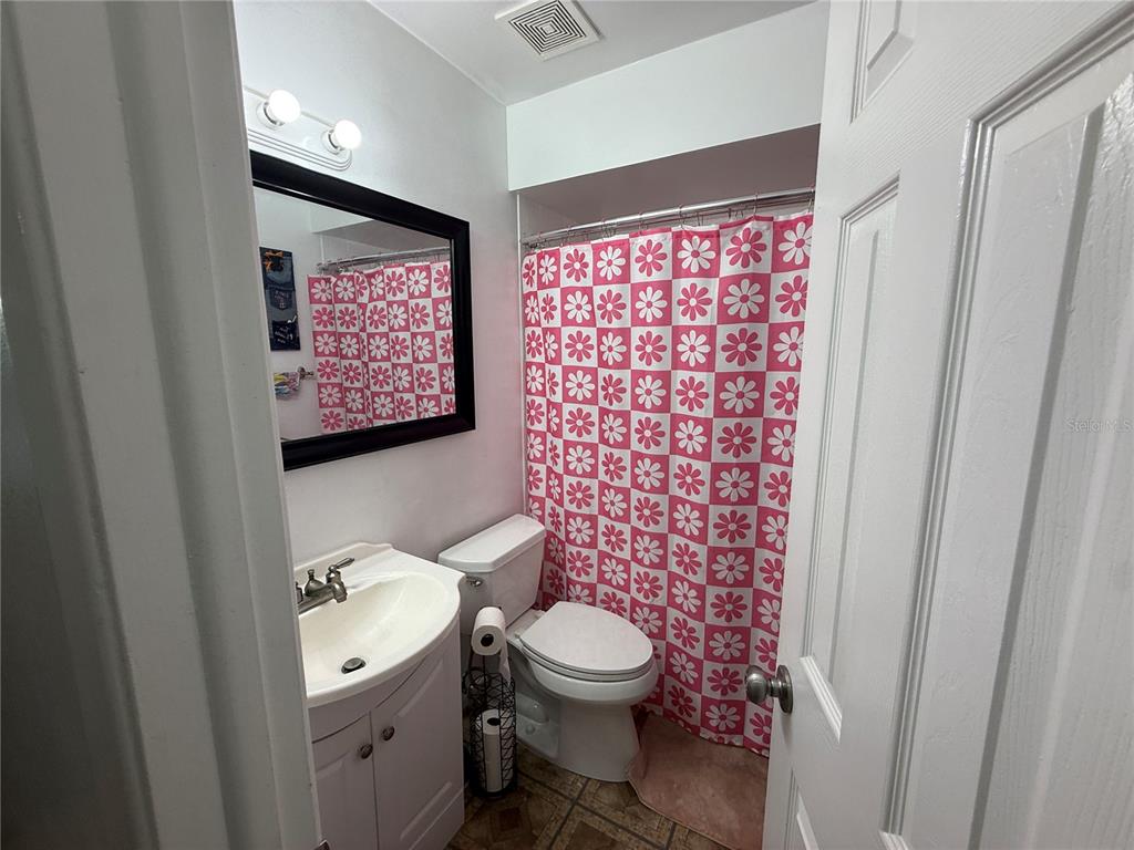 A small bathroom features a pedestal sink, a toilet, and a pink daisy-patterned shower curtain — 10009 REGAL WOODS LANE, TAMPA, FL