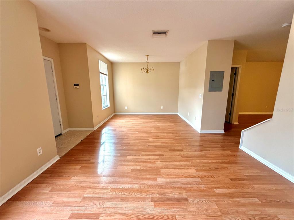 An empty room features light wood-look flooring, beige walls, and a central chandelier — 30209 SWINFORD LANE, WESLEY CHAPEL, FL
