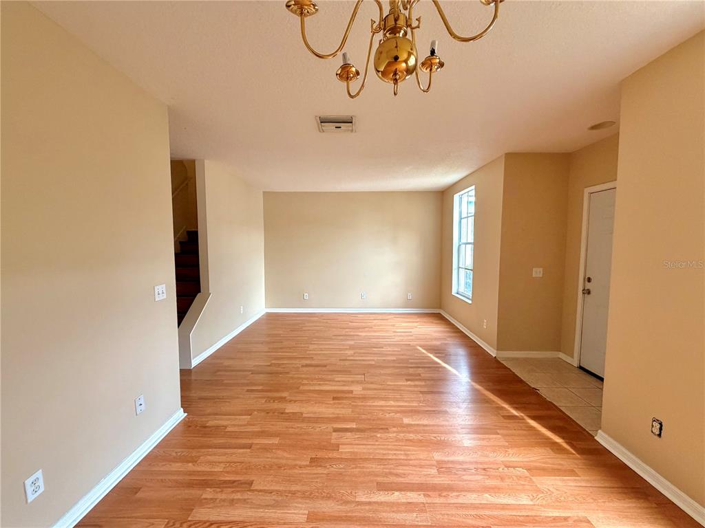 An empty room with wood-look flooring, beige walls, a chandelier, and a staircase — 30209 SWINFORD LANE, WESLEY CHAPEL, FL
