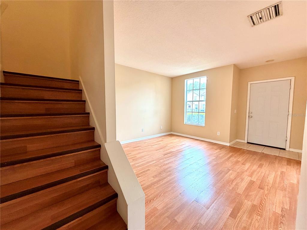 A room with wood-look flooring, a staircase on the left, and a front door — 30209 SWINFORD LANE, WESLEY CHAPEL, FL