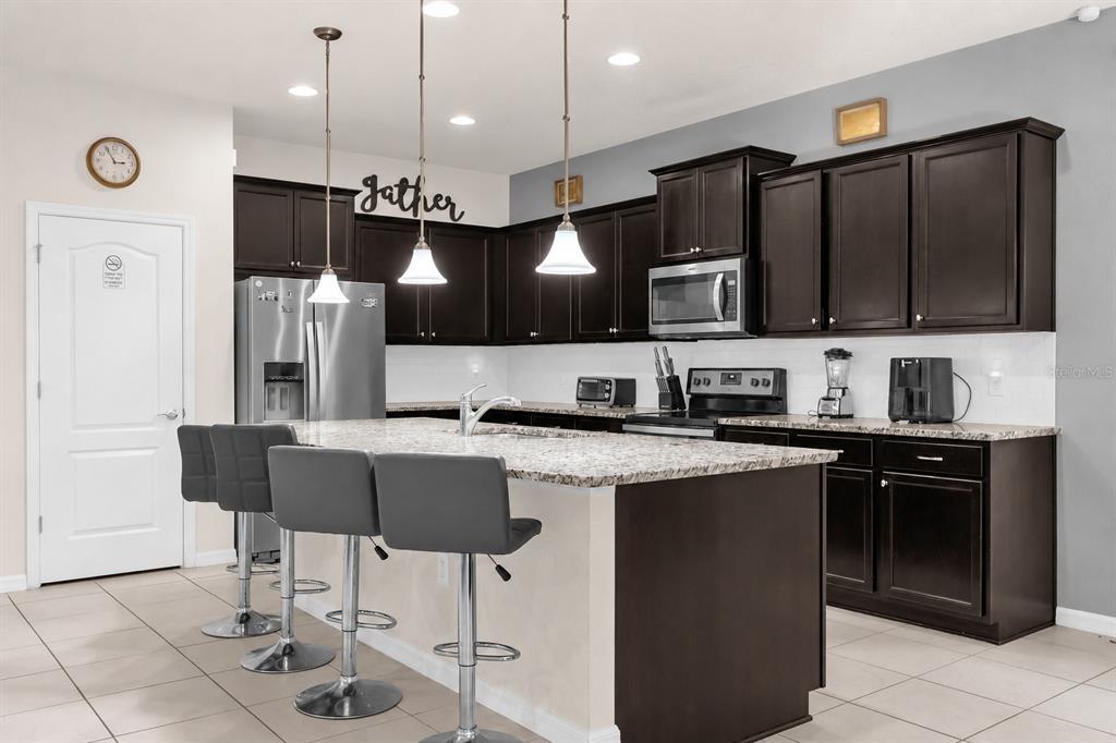 A kitchen features dark wood cabinets, granite countertops, a central island, and three bar stools — 8824 BENGAL COURT, KISSIMMEE, FL
